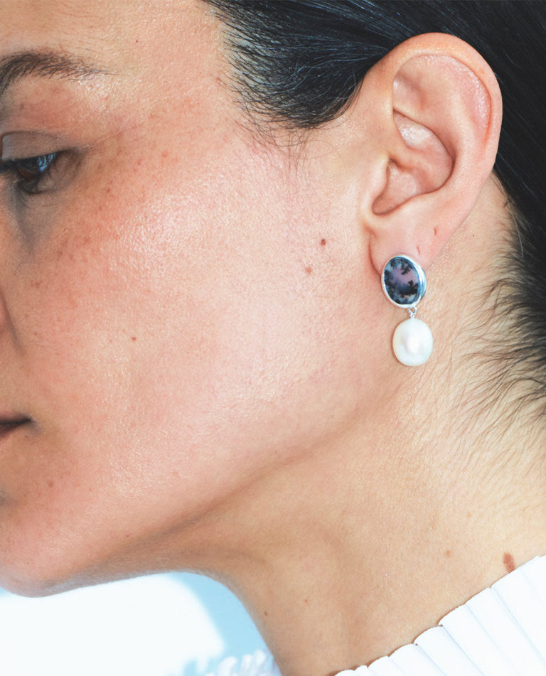 Close-up of a person wearing a pair of earrings with a white shirt in the background