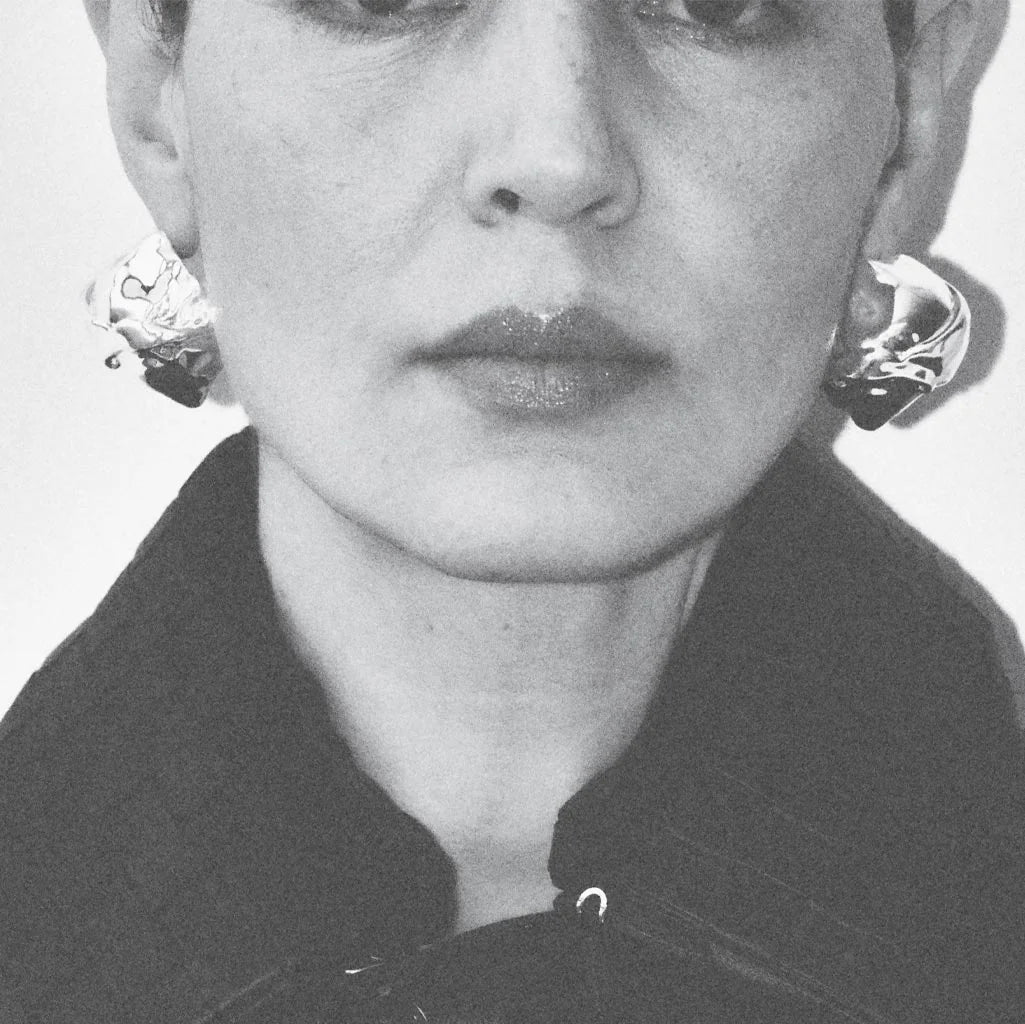 Black and white portrait of a person wearing earrings and a coat.