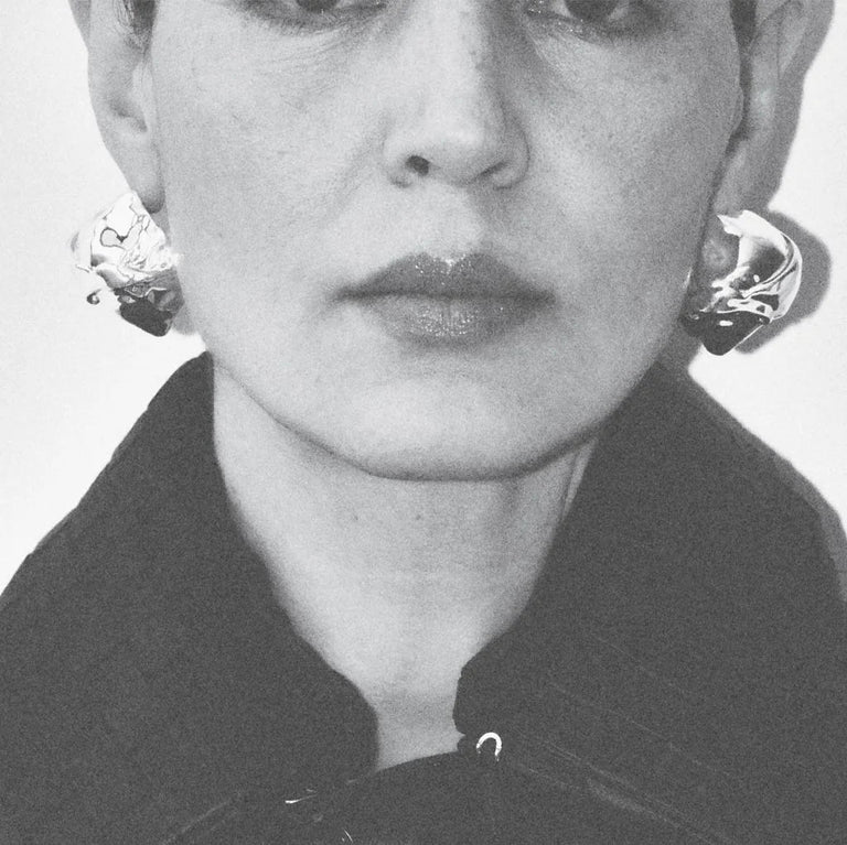 Black and white portrait of a person wearing earrings and a coat.